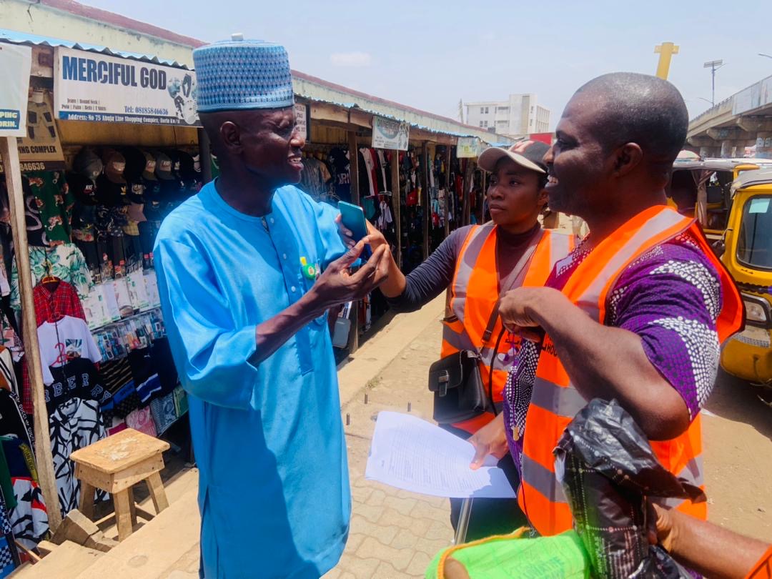 Salt House field officers in orange vests speaking with an elderly trader in a market